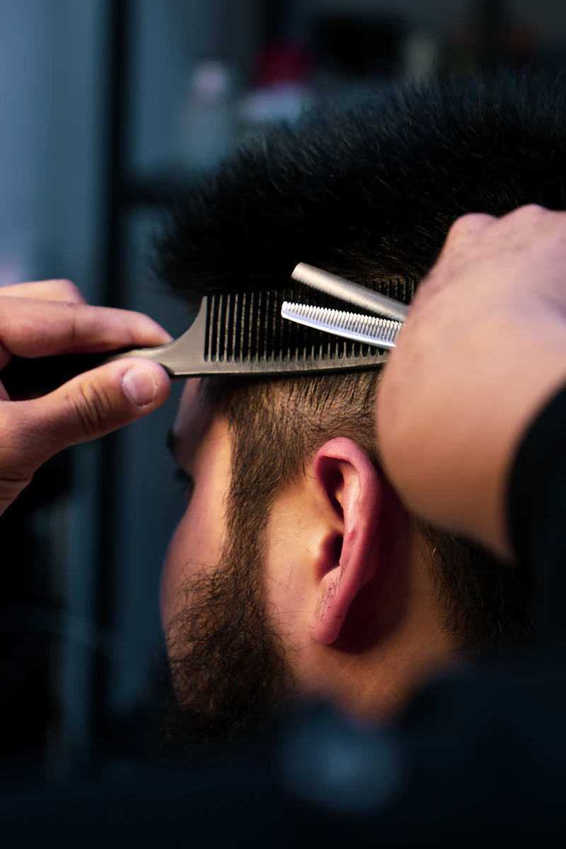 Kofi using thinning shears and a comb on a client's hair